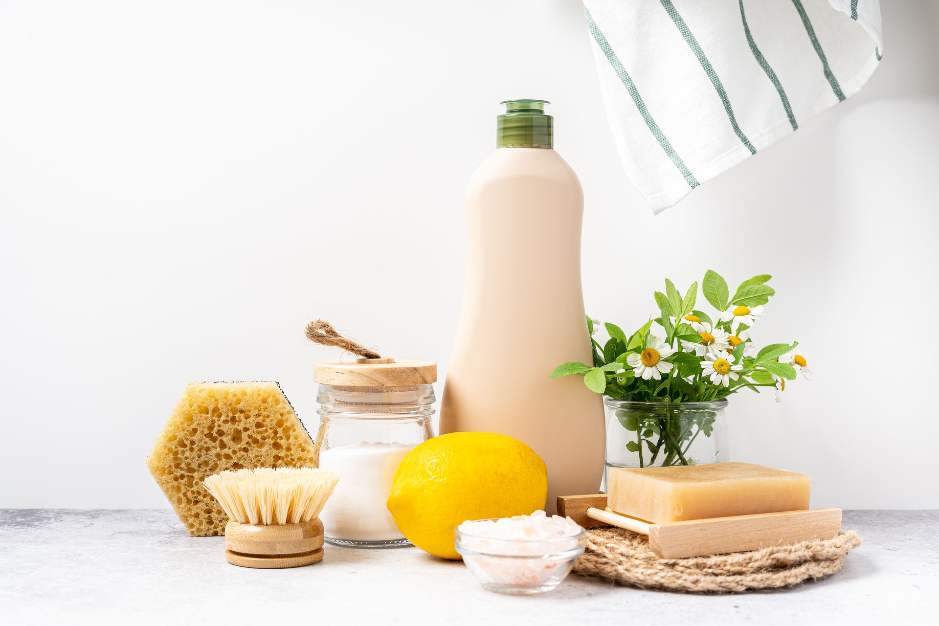 Eco friendly natural cleaners, jar with baking soda, dish brush, lemon, flowers, soap on white background. Organic ingredients for homemade cleans with mock up bottle. Zero waste concept, copy space