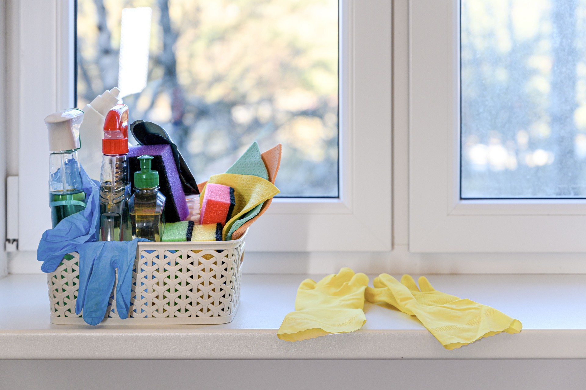 Spring house cleaning. Wicker basket with detergents on the windowsill.